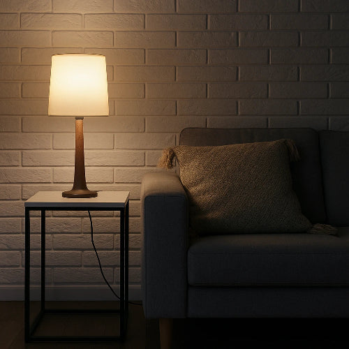 Dark living room with a lit table lamp and a sofa against a brick wall.